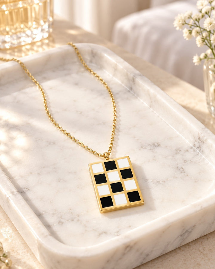 Elli Jewellery gold plated rectangular pendant necklace featuring a black and white checkered pattern on a marble tray