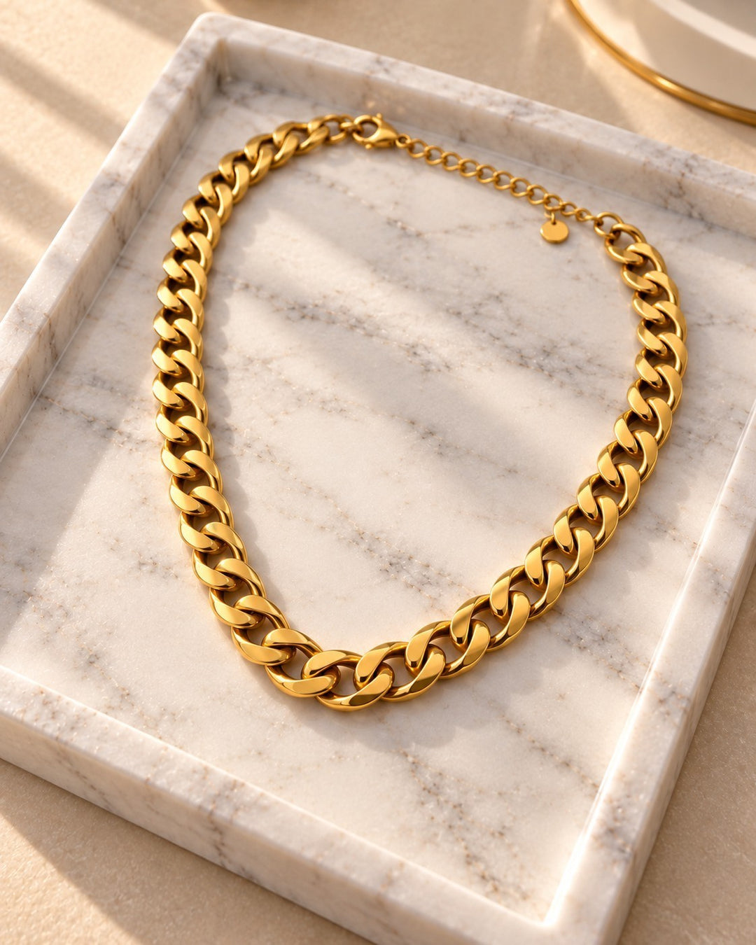 Elli Jewellery bold chunky gold-plated Cuban link chain necklace resting on a white marble tray