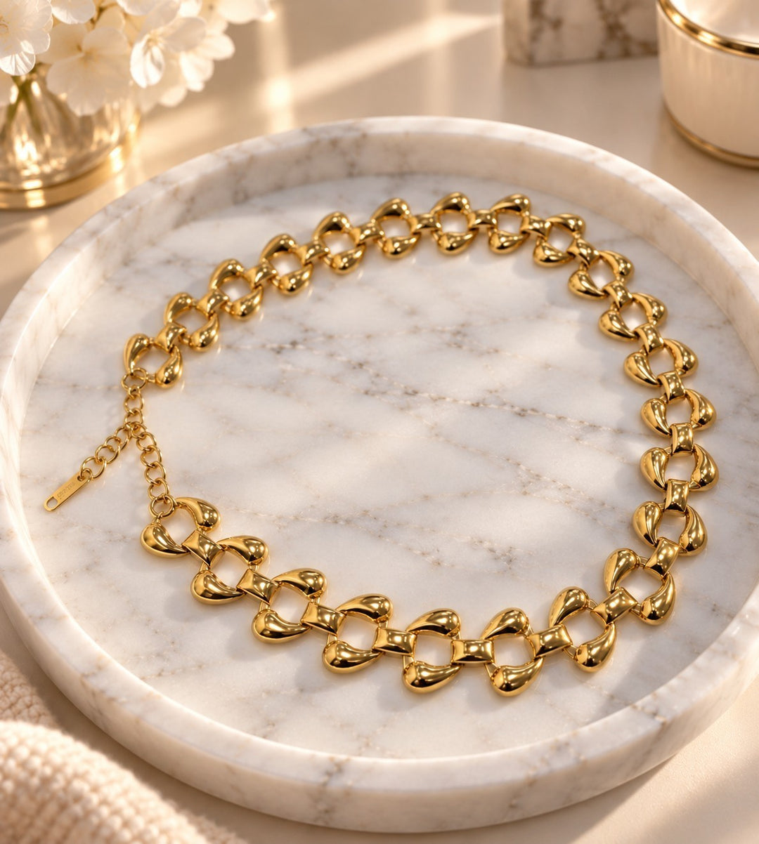 Elli Jewellery chunky curb chain necklace in 18ct gold plated metal with polished rounded links on a marble tray.