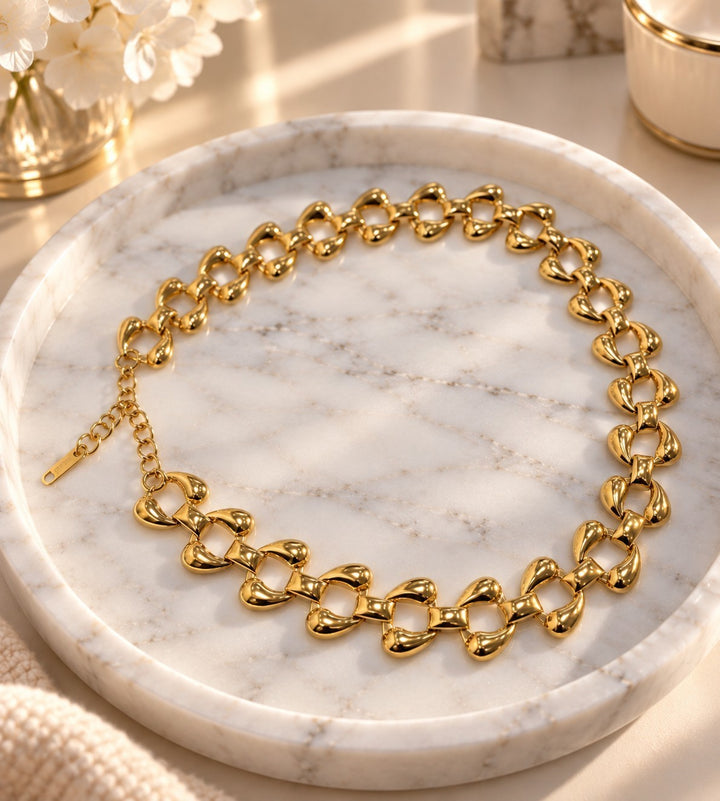 Elli Jewellery chunky curb chain necklace in 18ct gold plated metal with polished rounded links on a marble tray.