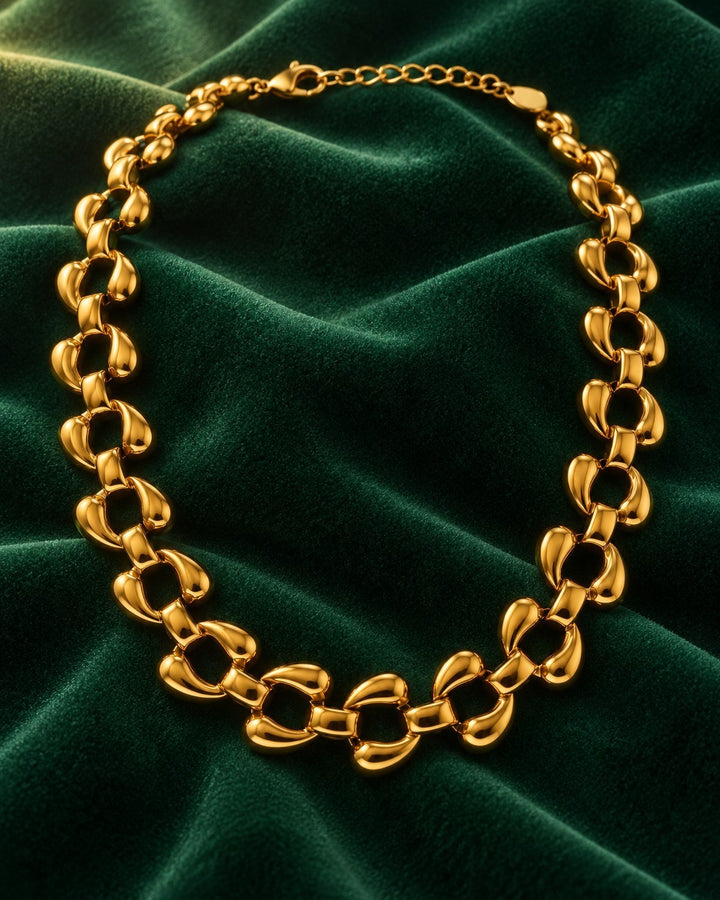 Elli Jewellery chunky gold-plated curb chain necklace with high-shine rounded links on a dark green velvet background.