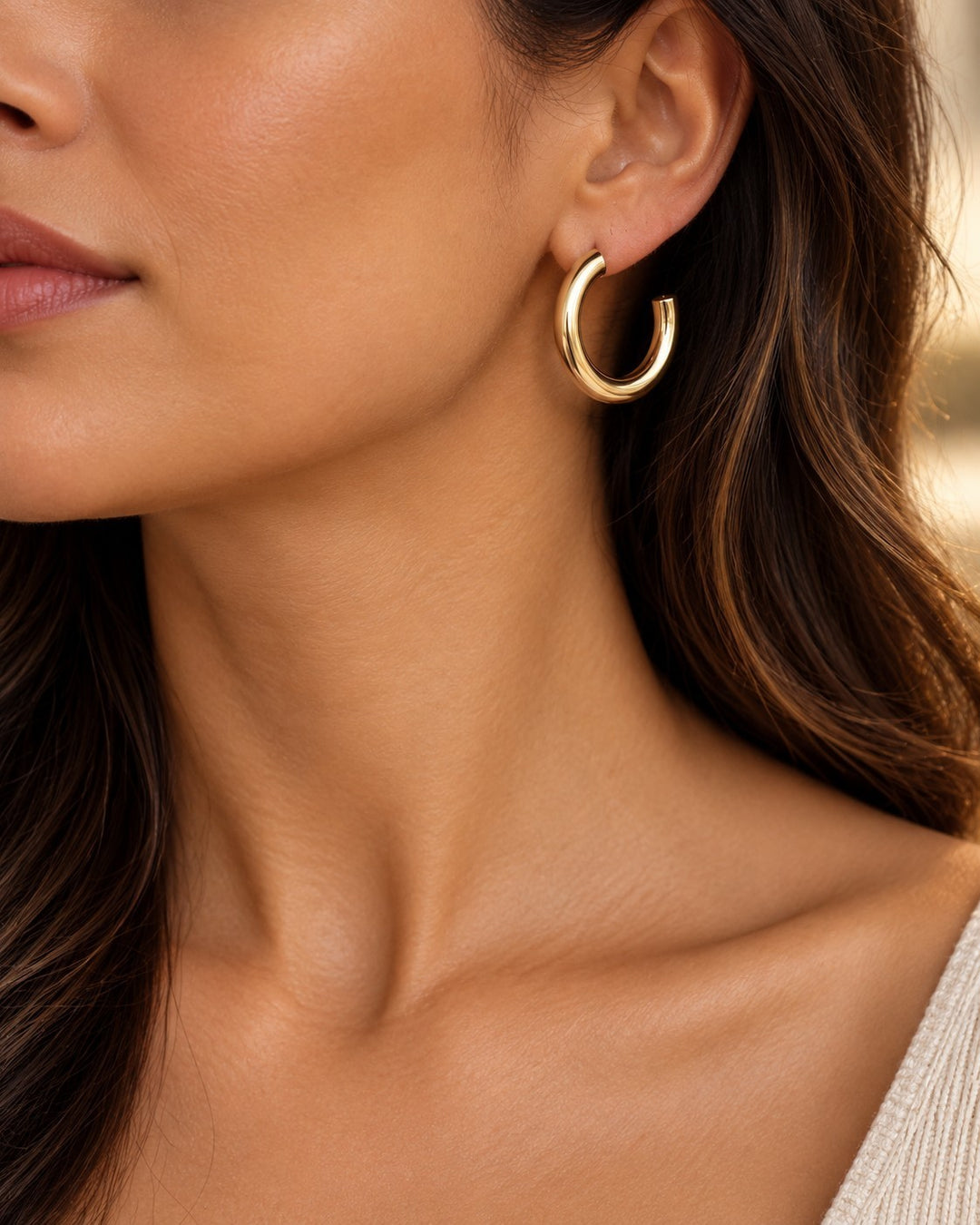 Elli Jewellery chunky gold plated hoop earrings worn by a woman with long wavy hair, featuring a polished finish.