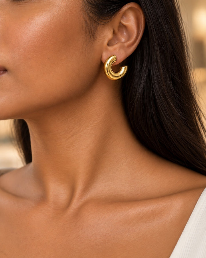 Elli Jewellery chunky C-shaped gold plated hoop earrings worn by a woman with dark hair