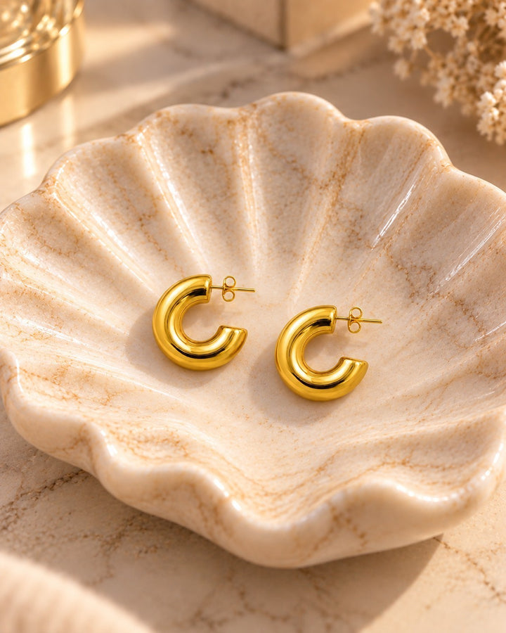 Elli Jewellery chunky C-shaped gold plated hoop earrings resting in a decorative ceramic shell dish