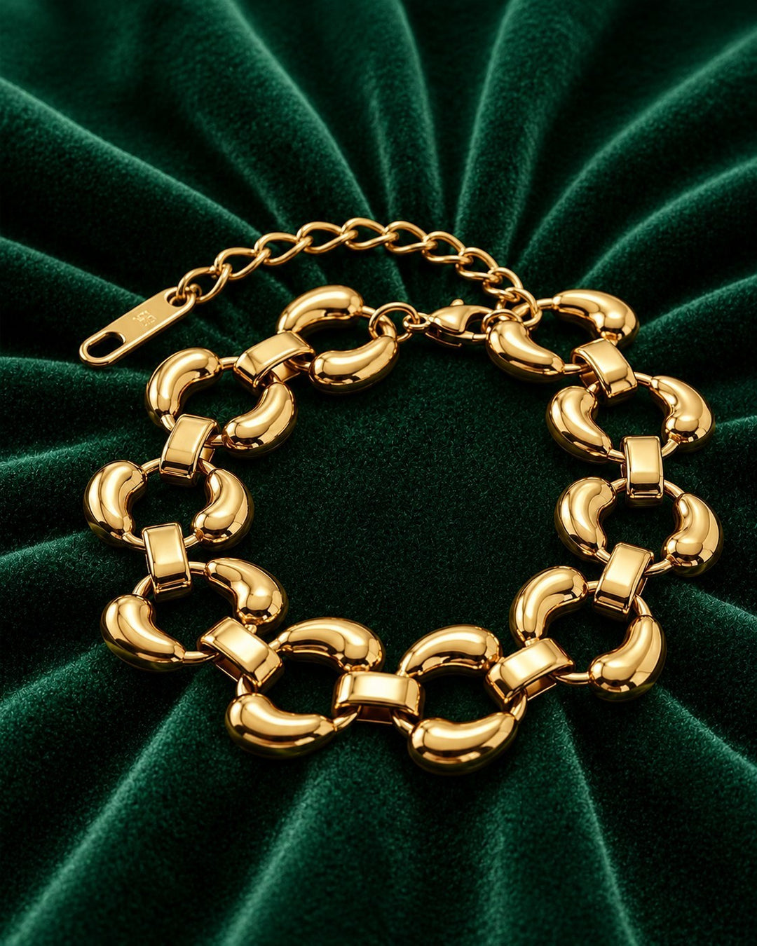 Elli Jewellery chunky oval link bracelet in 18ct gold plated finish resting on a dark green velvet background