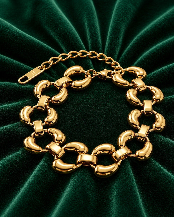 Elli Jewellery chunky oval link bracelet in 18ct gold plated finish resting on a dark green velvet background