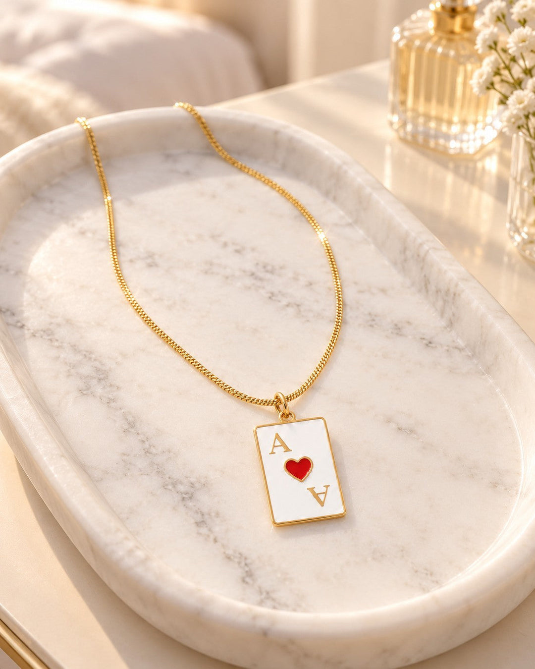 Elli Jewellery gold plated Ace of Hearts playing card pendant necklace on a white marble tray.