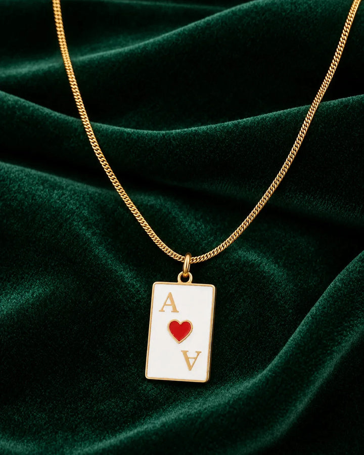 Elli Jewellery gold plated Ace of Hearts playing card pendant necklace on a dark green velvet background