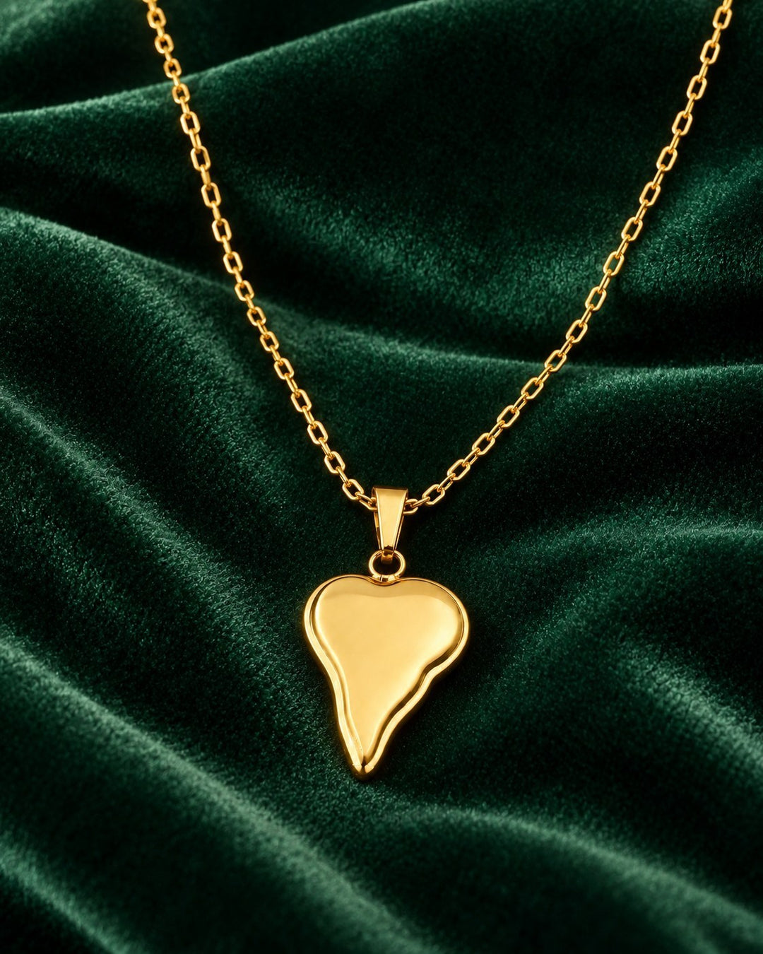 Elli Jewellery gold plated asymmetric heart pendant necklace on a dark green velvet background