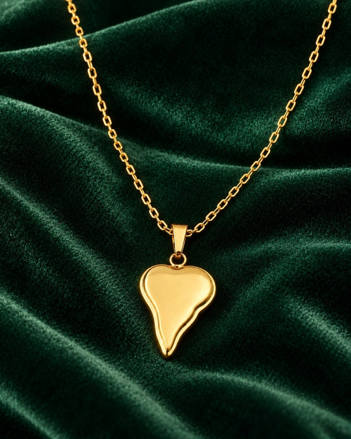 Elli Jewellery gold plated asymmetric heart pendant necklace on a dark green velvet background