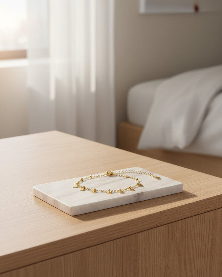 Elli Jewellery gold toned ball anklet with delicate chain on a white marble display stand in a bedroom setting