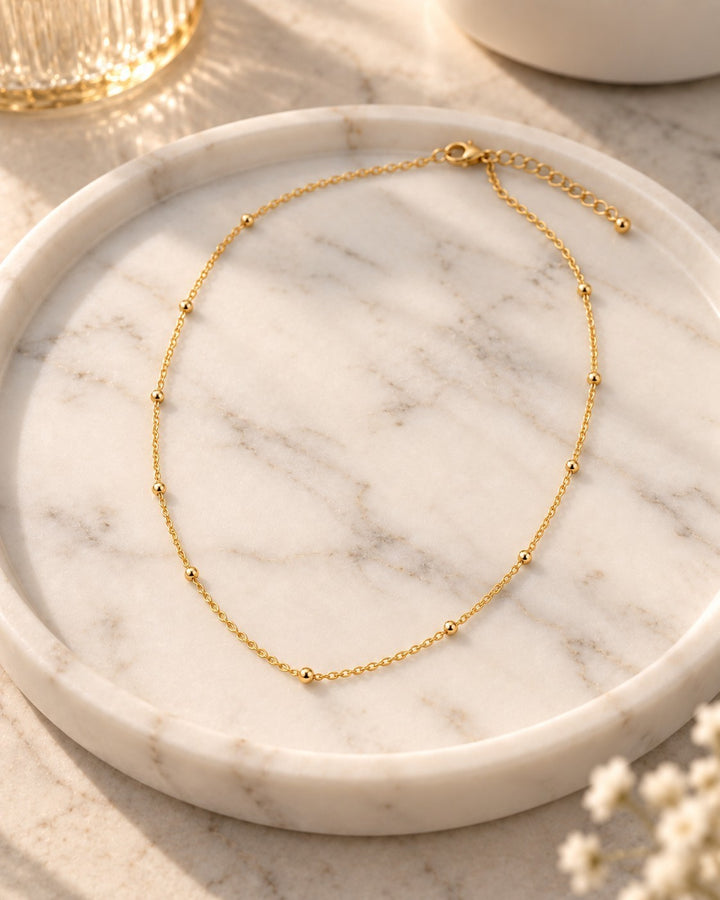 Elli Jewellery gold plated dainty ball bead chain necklace resting on a white marble tray
