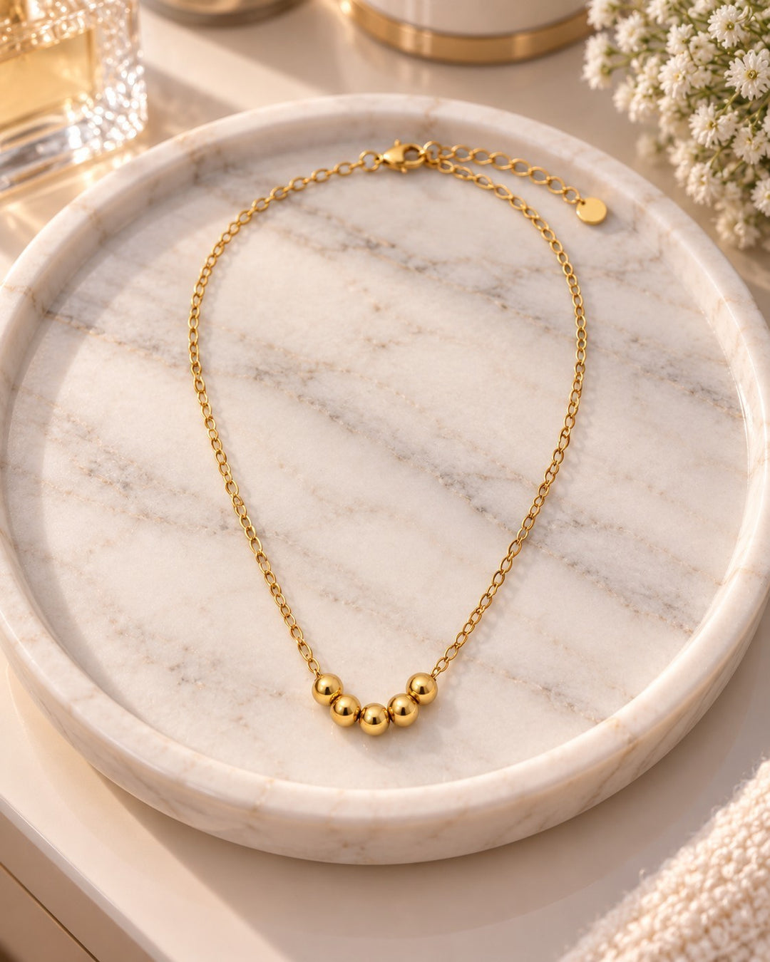 Elli Jewellery gold plated waterproof necklace with five spherical ball charms on a delicate chain, on marble tray.