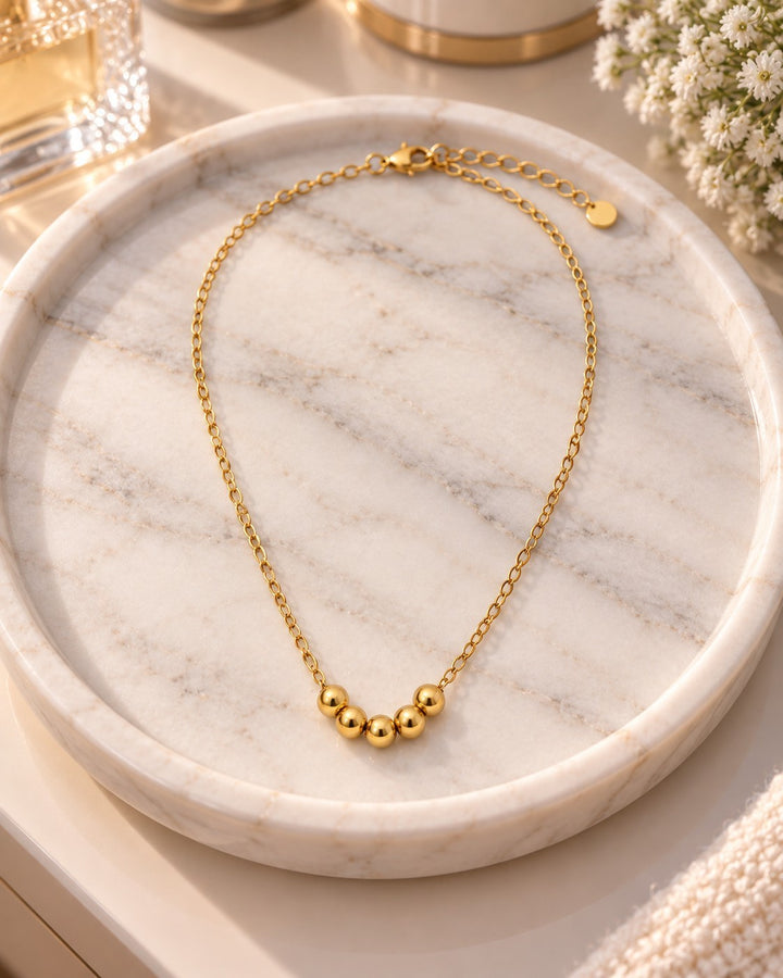 Elli Jewellery gold plated waterproof necklace with five spherical ball charms on a delicate chain, on marble tray.