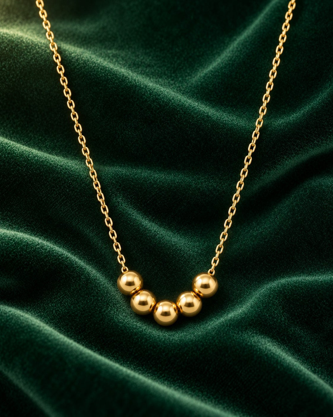 Elli Jewellery gold plated waterproof necklace with five spherical ball charms on a delicate chain against green velvet
