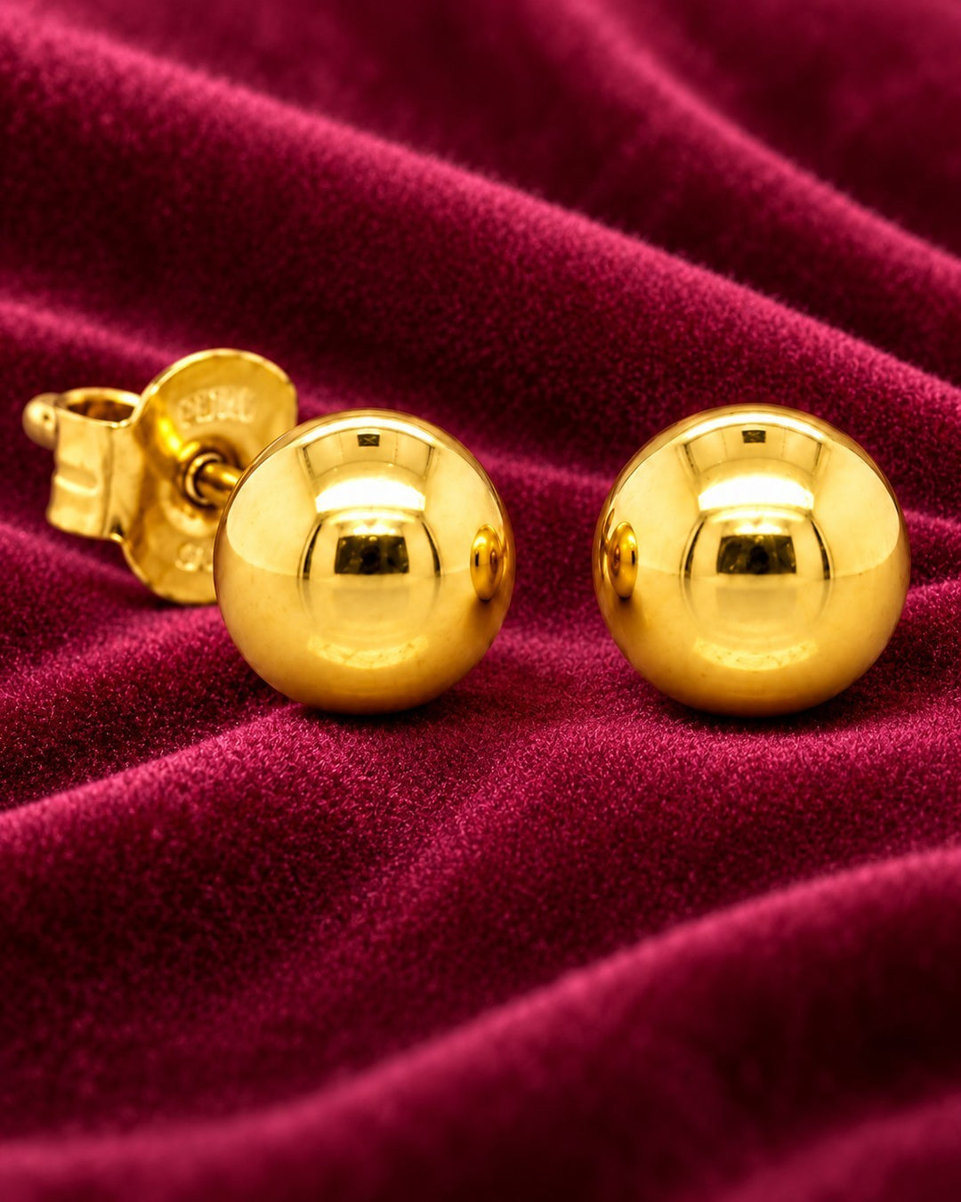 Elli Jewellery minimalist gold plated small ball stud earrings on a luxurious deep red velvet background