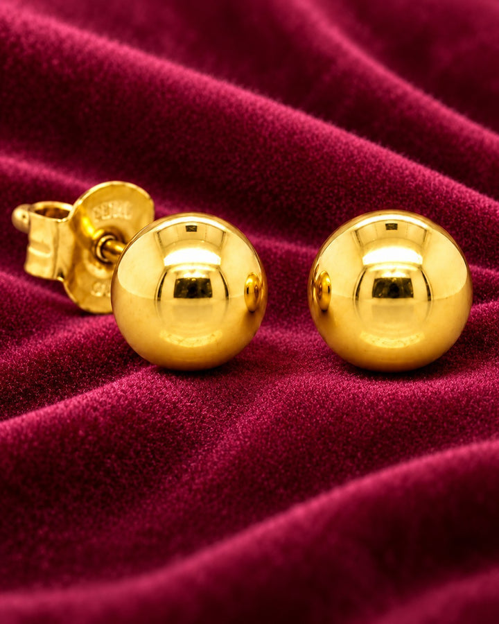 Elli Jewellery minimalist gold plated small ball stud earrings on a luxurious deep red velvet background