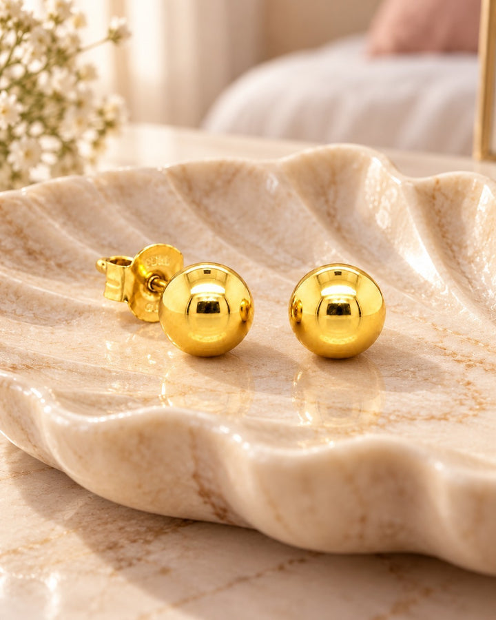 Elli Jewellery minimalist gold plated ball stud earrings resting on a decorative shell dish
