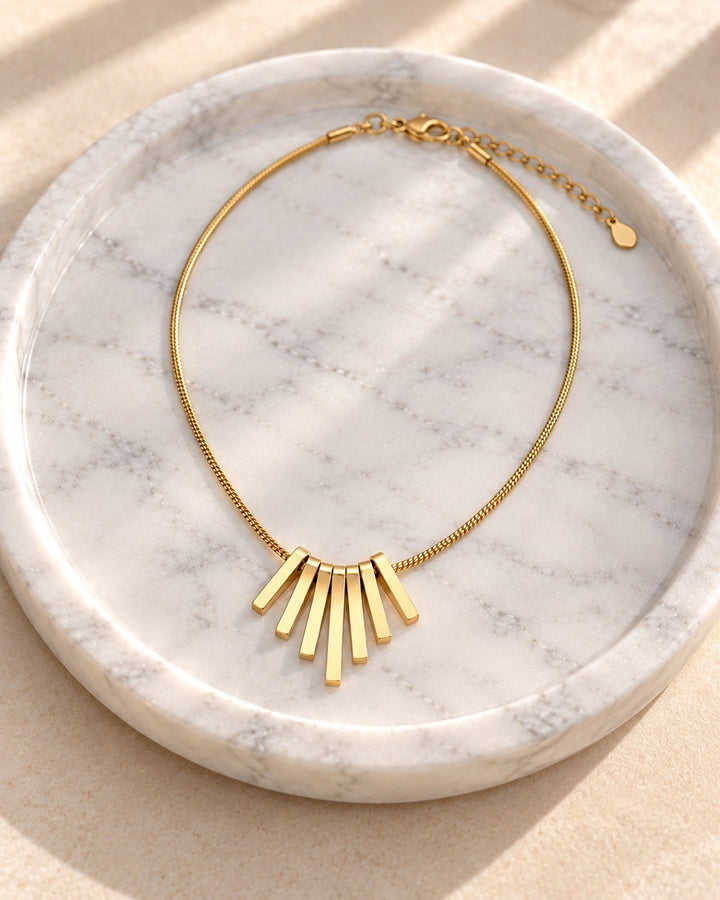 Elli Jewellery gold plated necklace featuring a geometric bar pendant on a delicate chain, displayed on marble tray.