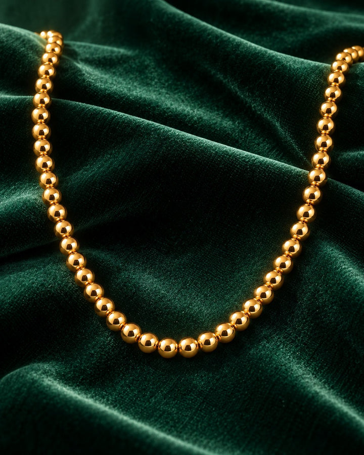 Elli Jewellery gold-plated waterproof beaded ball chain necklace resting on a luxurious dark green velvet background.