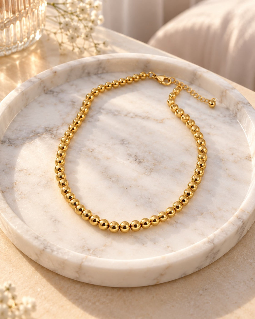 Elli Jewellery gold-plated waterproof beaded ball chain necklace resting on a white marble tray in soft sunlight.