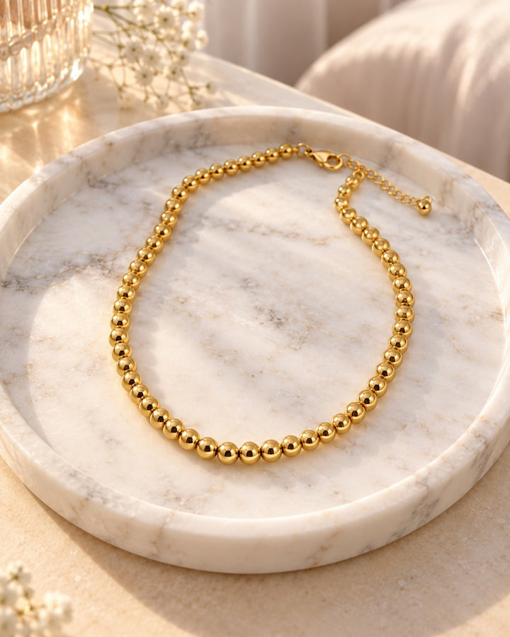 Elli Jewellery gold-plated waterproof beaded ball chain necklace resting on a white marble tray in soft sunlight.