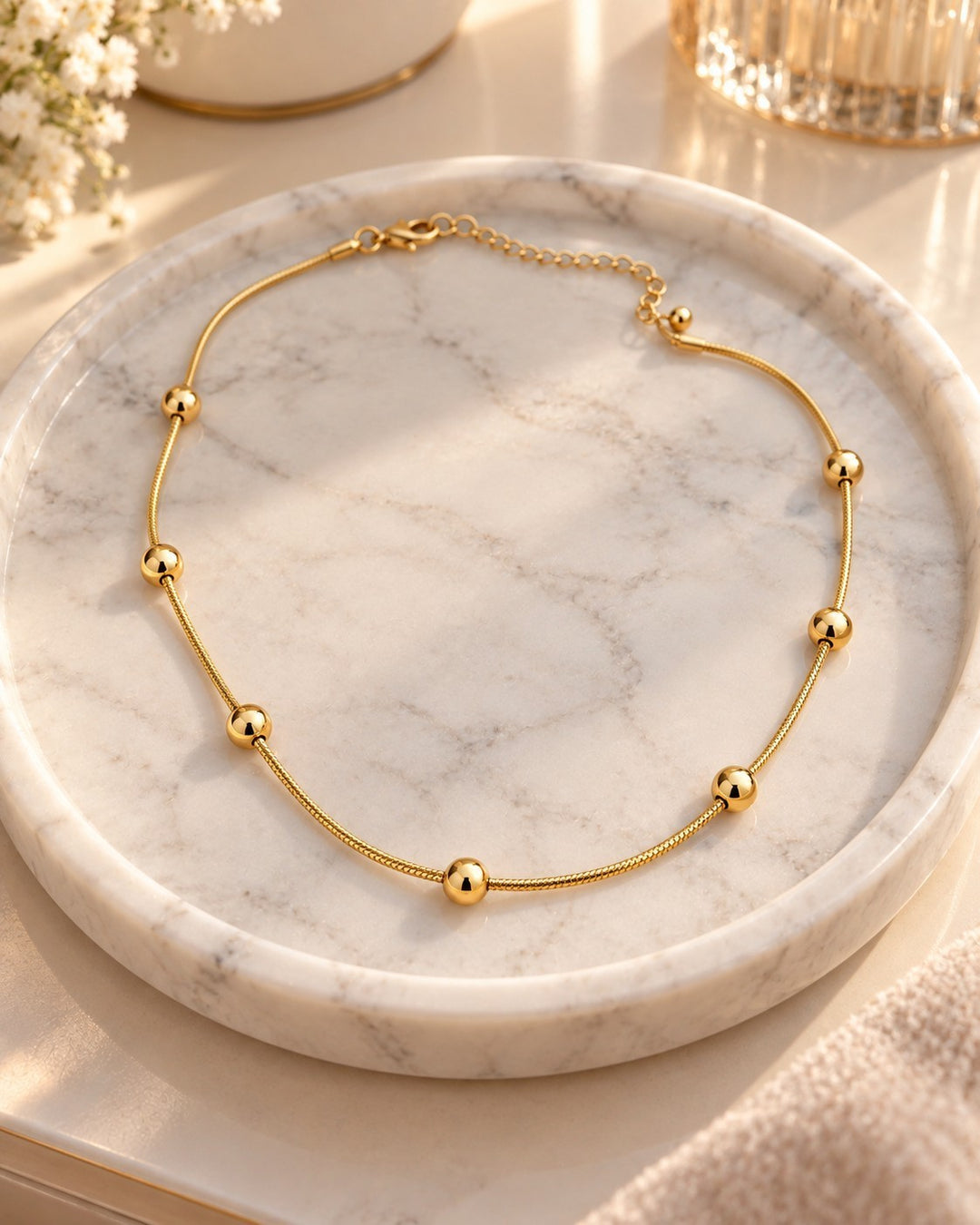Elli Jewellery gold plated waterproof chain necklace with delicate beads resting on a white marble tray.