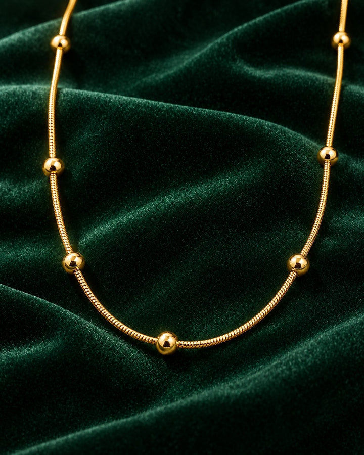 Elli Jewellery gold plated waterproof snake chain necklace with delicate beads on a dark green velvet background