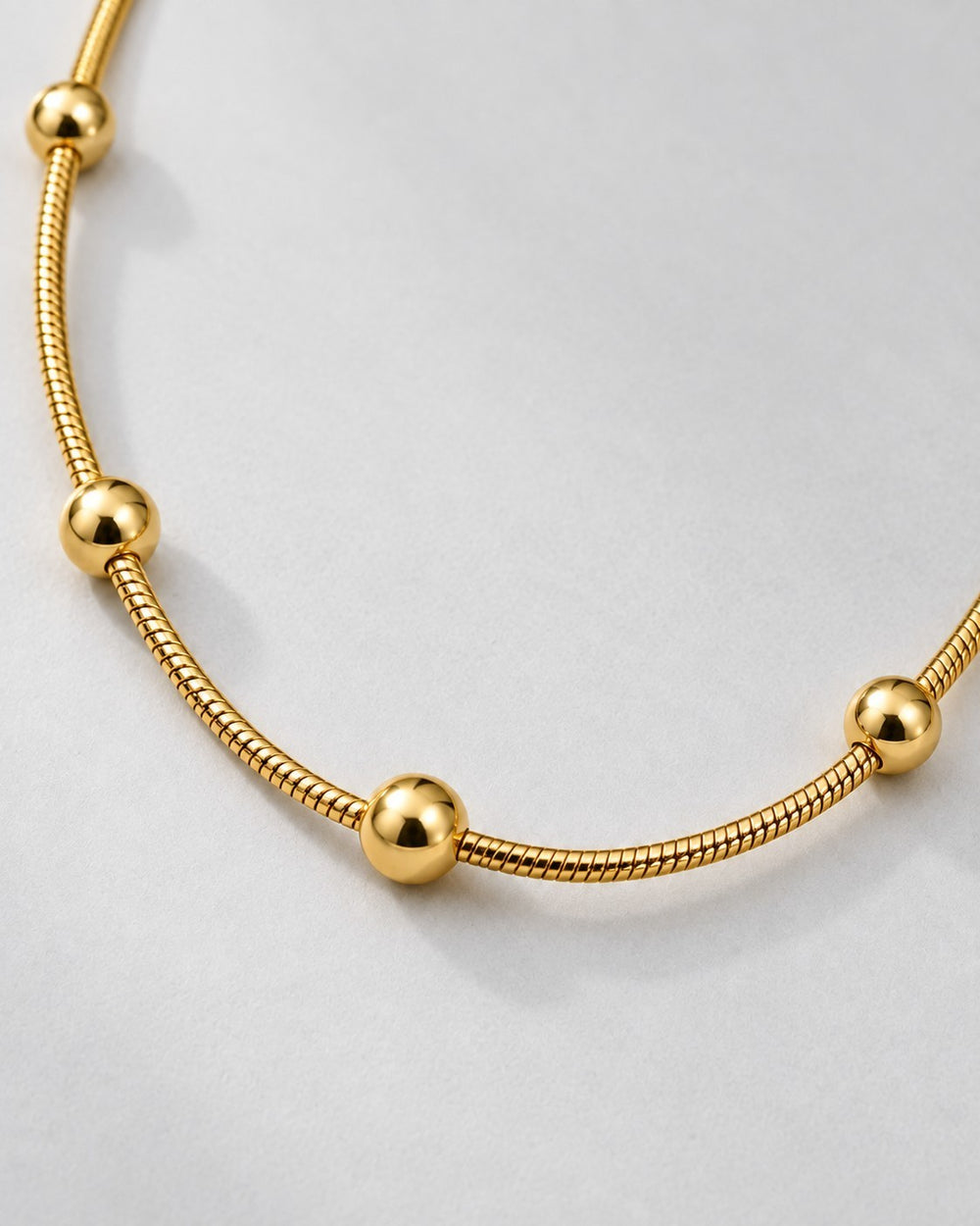 Elli Jewellery gold plated waterproof snake chain necklace with polished spherical beads on a light grey background.