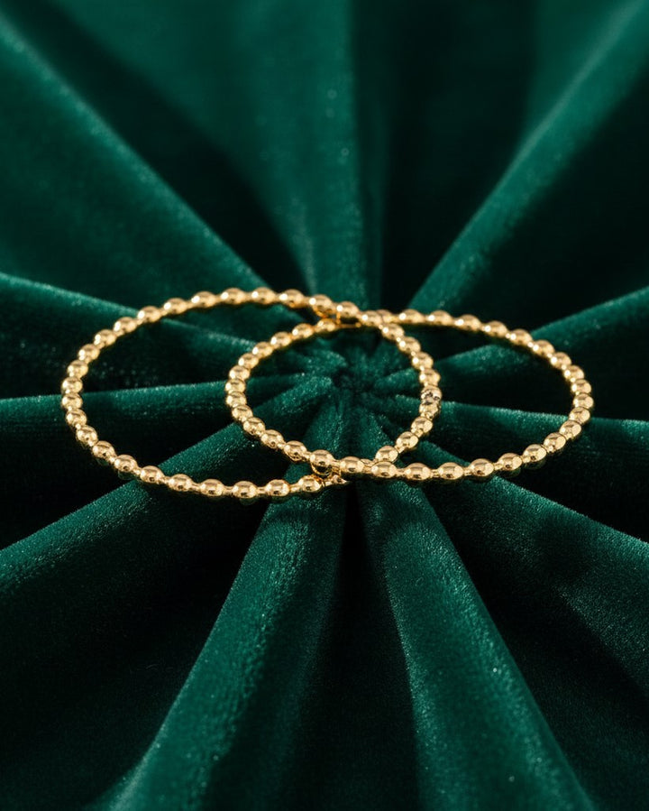 Elli Jewellery gold plated double stack ring with a delicate beaded texture resting on dark green velvet fabric.