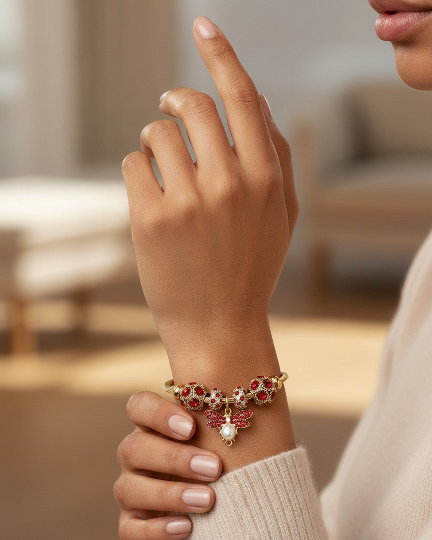 Elli Jewellery gold plated hinged bangle featuring a red crystal bee charm and matching decorative beads on a wrist