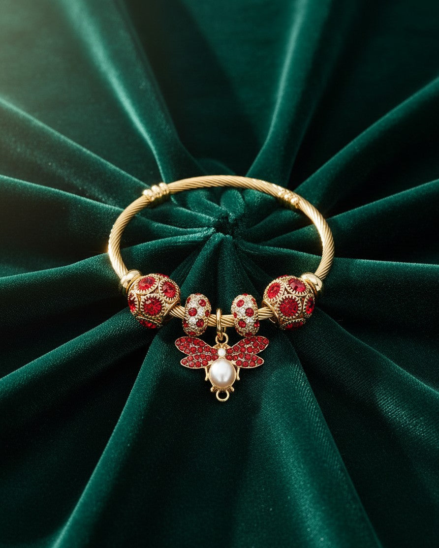 Elli Jewellery gold plated hinged bangle featuring a bee charm with red crystals and a pearl on green velvet.