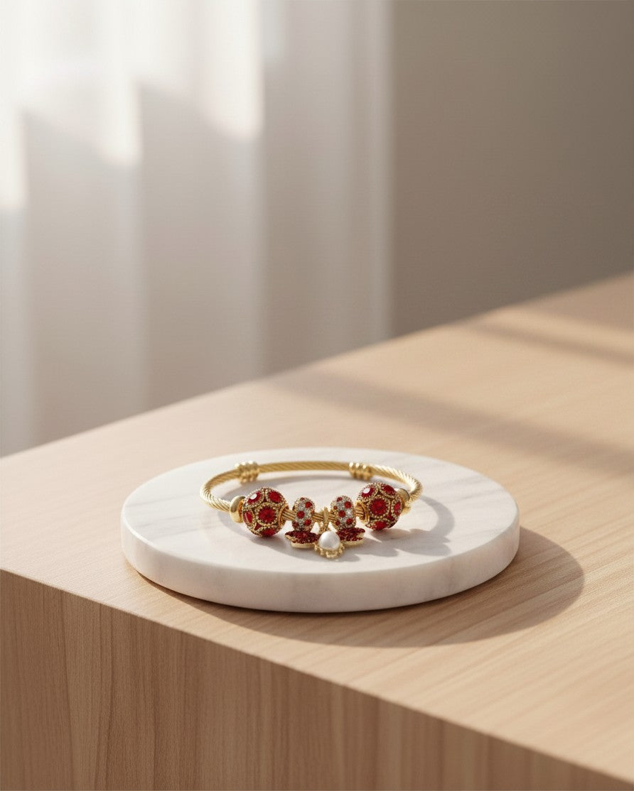 Elli Jewellery gold plated hinged bangle featuring a bee charm and red beaded accents on a white marble display stand.