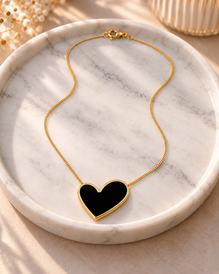 Elli Jewellery gold plated necklace featuring a glossy black enamel heart pendant on a delicate chain on marble tray