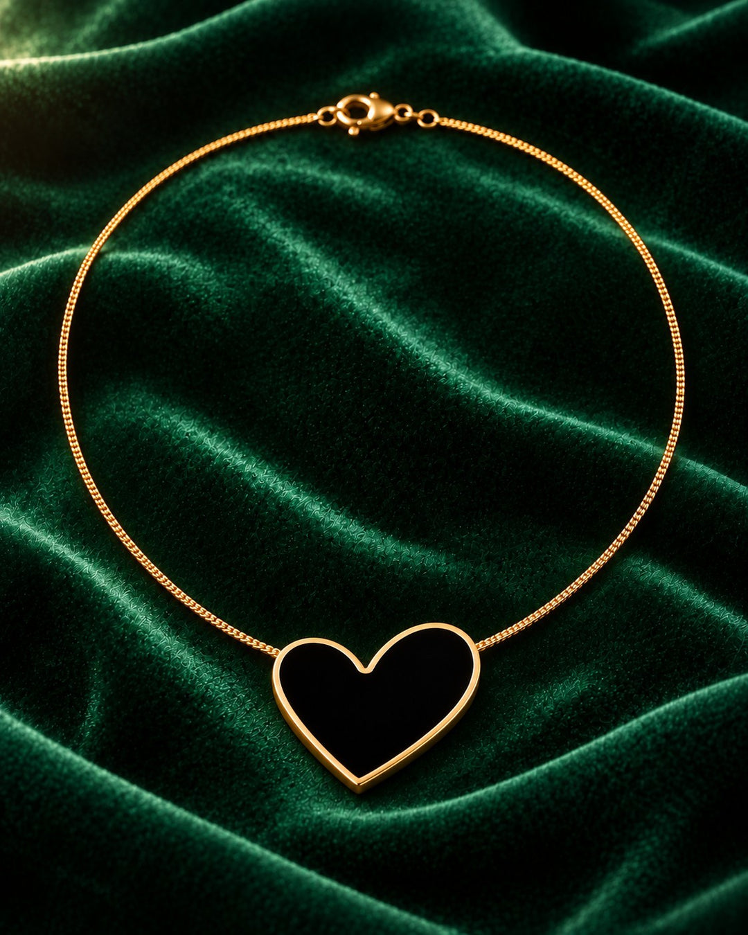 Elli Jewellery gold plated necklace featuring a black enamel heart pendant on a delicate chain against green velvet.