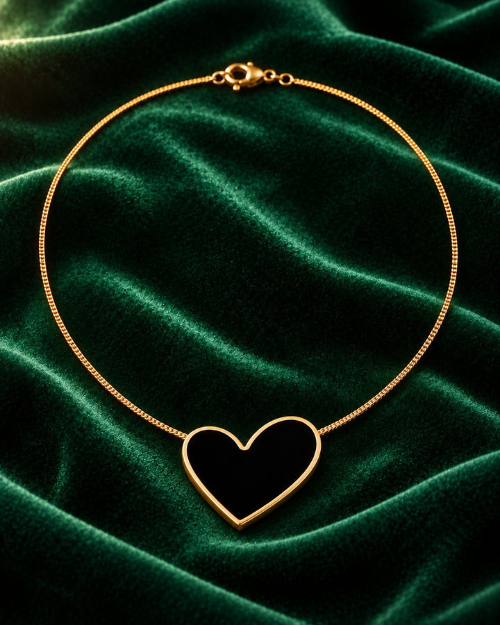 Elli Jewellery gold plated necklace featuring a black enamel heart pendant on a delicate chain against green velvet.