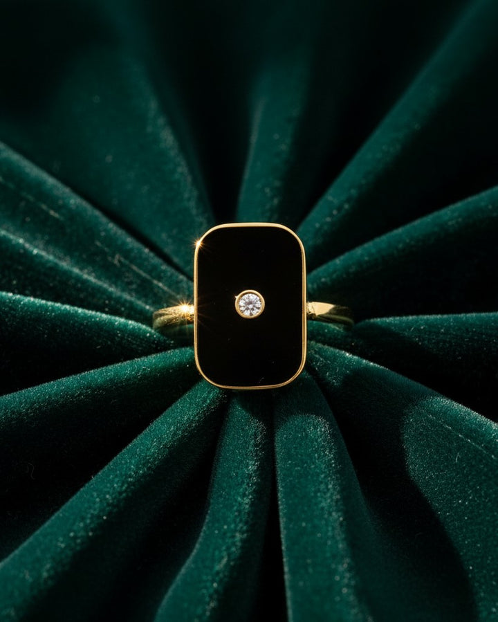 Elli Jewellery gold-plated rectangular statement ring with black enamel and a central sparkling stone on green velvet.