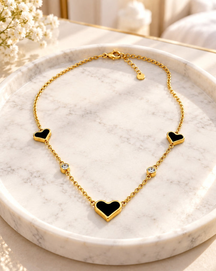 Elli Jewellery gold plated necklace featuring three black heart pendants and two clear crystal accents on a chain.