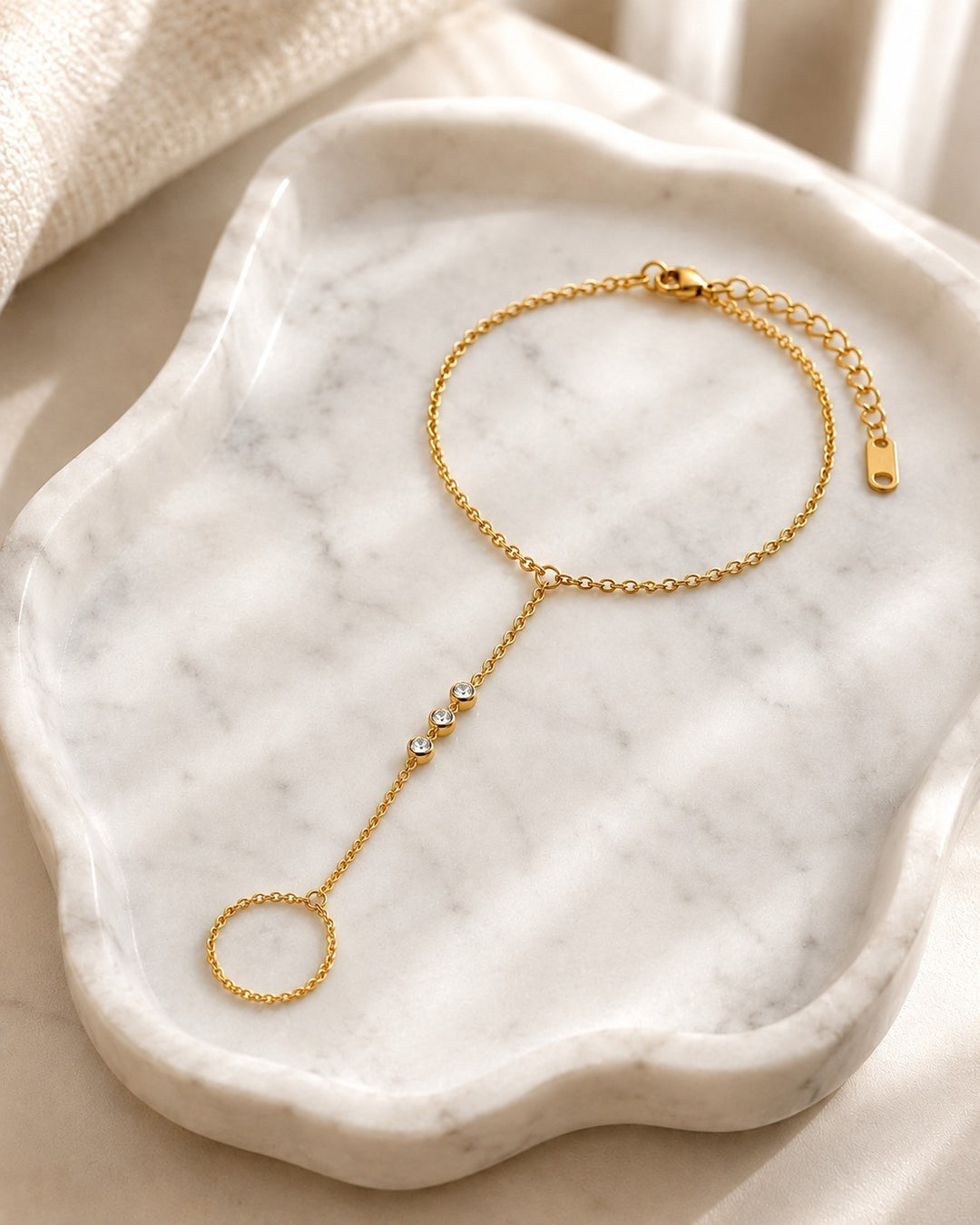 Elli Jewellery gold plated boho hand chain bracelet with three small crystals on a white marble tray