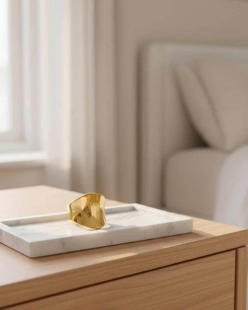 Elli Jewellery gold plated brushed cambered open cuff ring resting on a white marble tray in a minimalist bedroom.