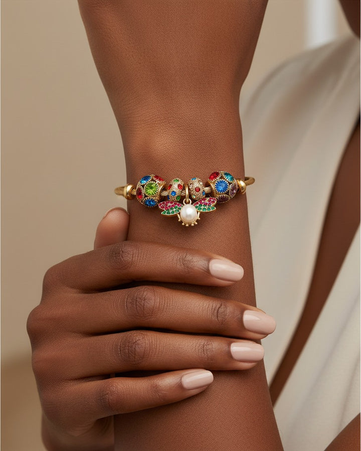 Elli Jewellery gold plated bangle featuring red and green enamel butterfly charms with a central pearl on a wrist