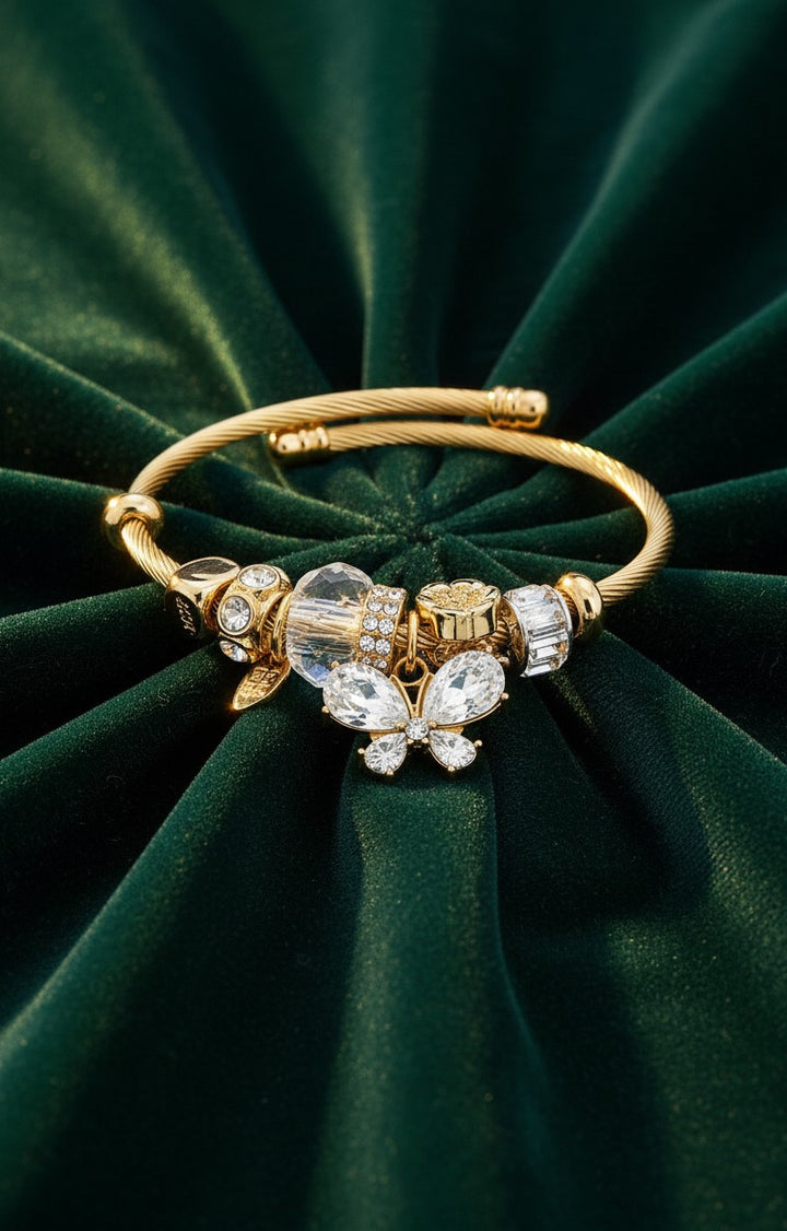 Elli Jewellery gold plated bangle featuring a sparkling diamanté butterfly charm on a dark green velvet background.