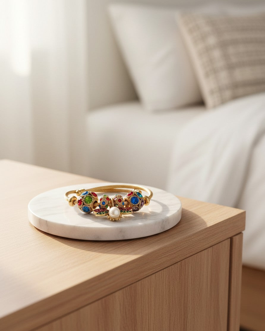 Elli Jewellery gold plated bangle featuring red and green enamel butterfly charms and a central pearl on a marble tray