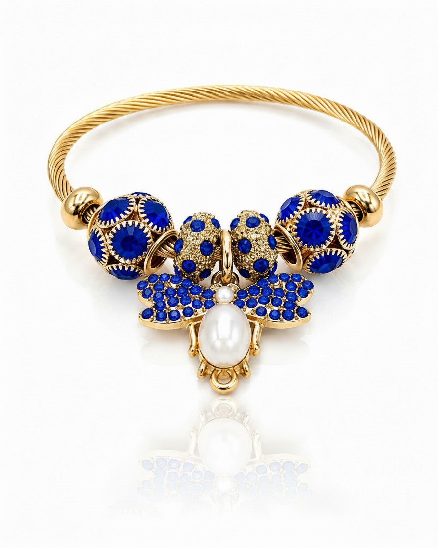 Elli Jewellery gold plated bangle featuring a blue butterfly charm with a central pearl and blue crystal accents.