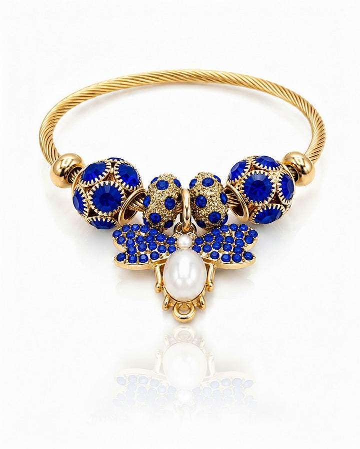 Elli Jewellery gold plated bangle featuring a blue butterfly charm with a central pearl and blue crystal accents.