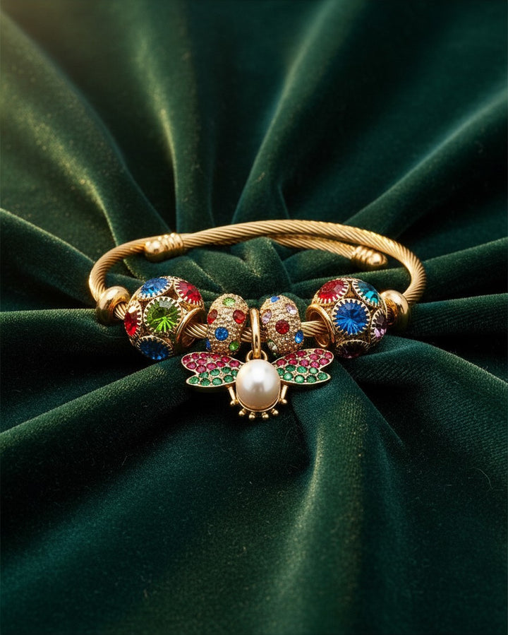 Elli Jewellery gold plated bangle featuring a pearl butterfly charm with red and green enamel on green velvet.