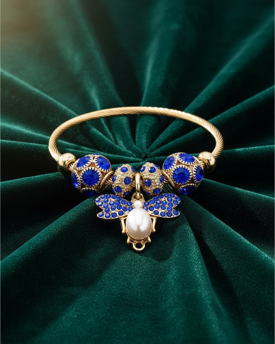 Elli Jewellery gold plated bangle featuring a blue butterfly charm with crystals and a central pearl on green velvet.