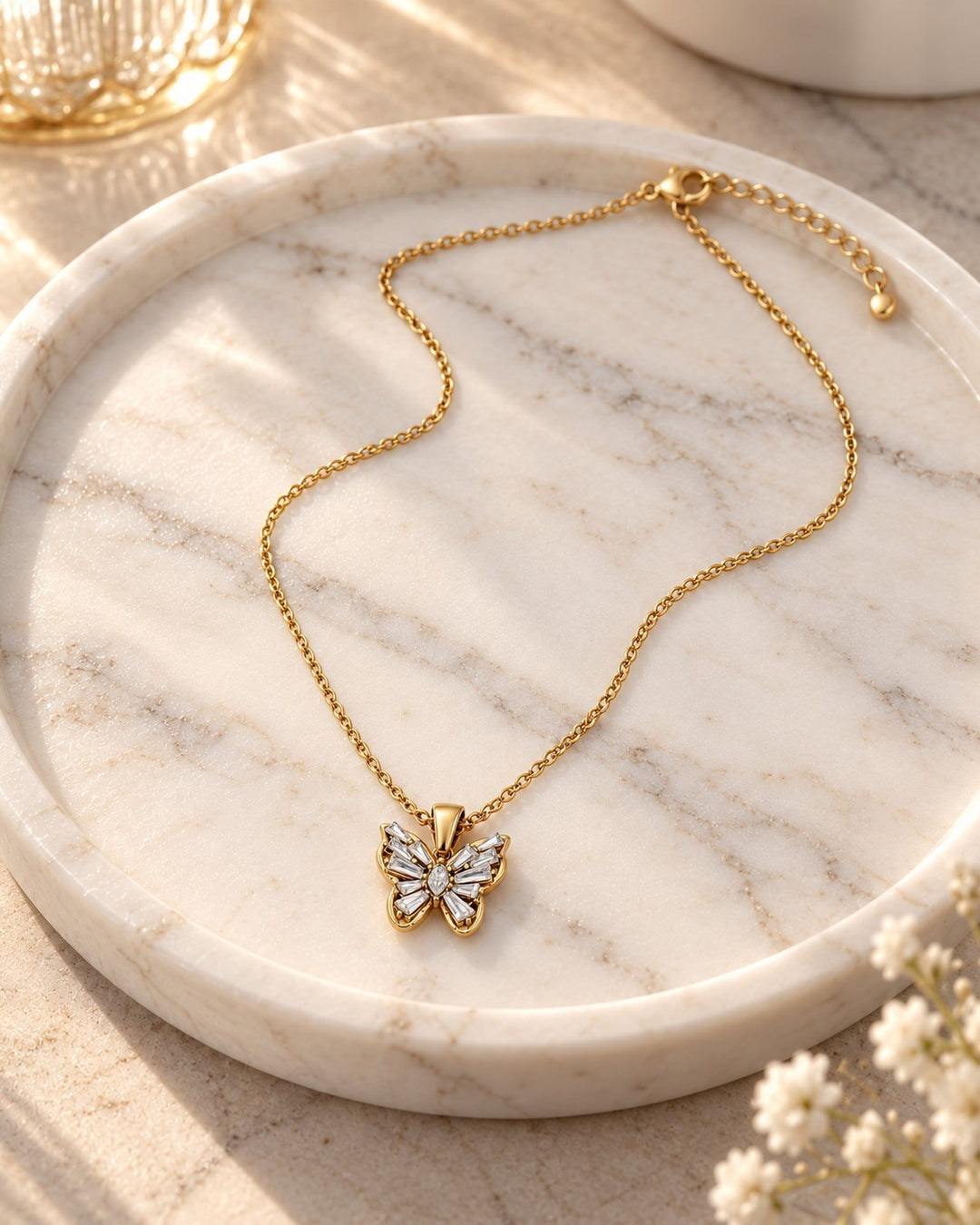 Elli Jewellery gold plated butterfly pendant necklace with sparkling cubic zirconia stones on a marble tray.