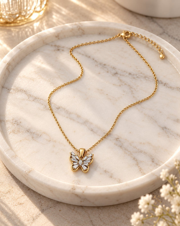 Elli Jewellery gold plated butterfly pendant necklace with sparkling cubic zirconia stones on a marble tray.
