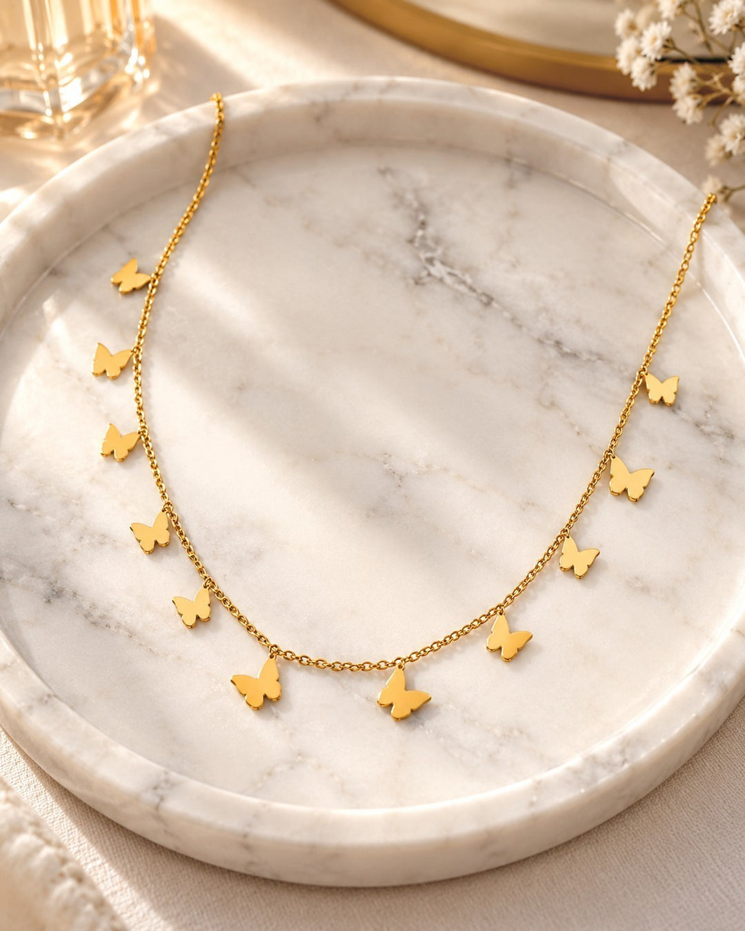 Elli Jewellery gold plated waterproof delicate chain necklace featuring multiple small butterfly charms on marble tray